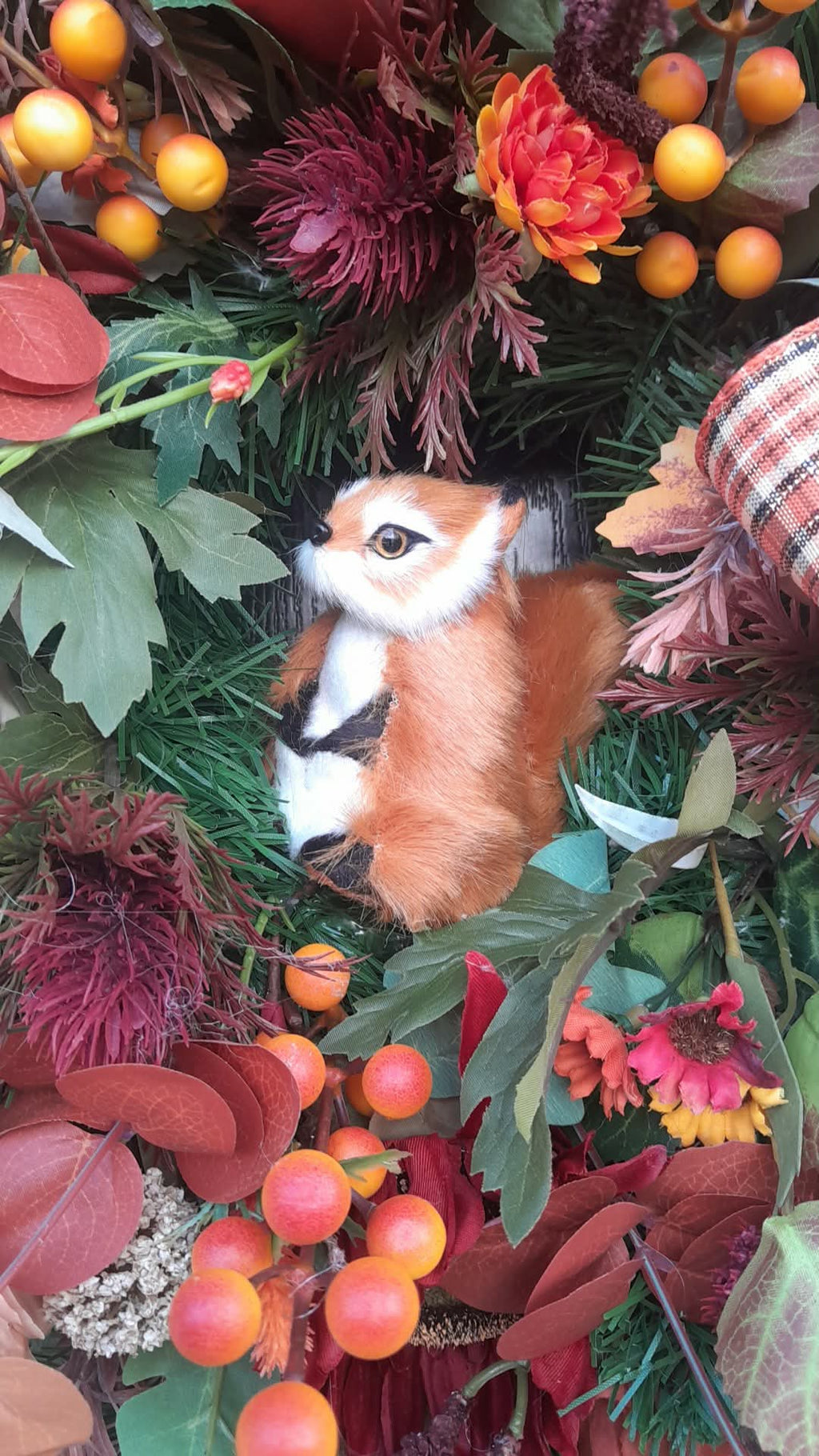 Close-up of fox figurine nestled amongst berries and autumn blooms