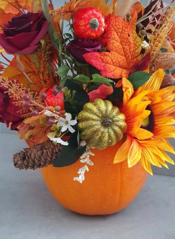 Hallow pumpkin autumn arrangement close up - deep burgundy roses, sunflower, mini pumpkins, pine cones and autumn foliage