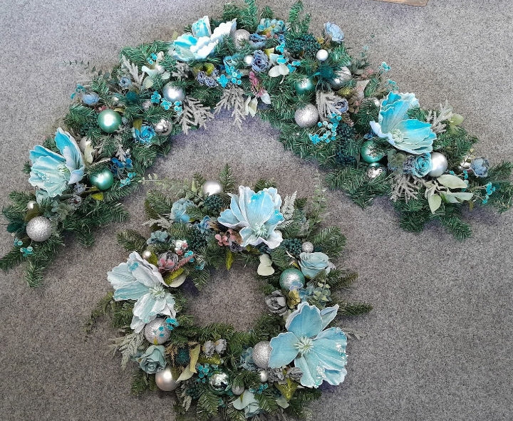 Teal and silver Christmas 6ft garland and matching wreath set laid out on a grey floor with teal magnolia blooms, silver baubles and snowflake details