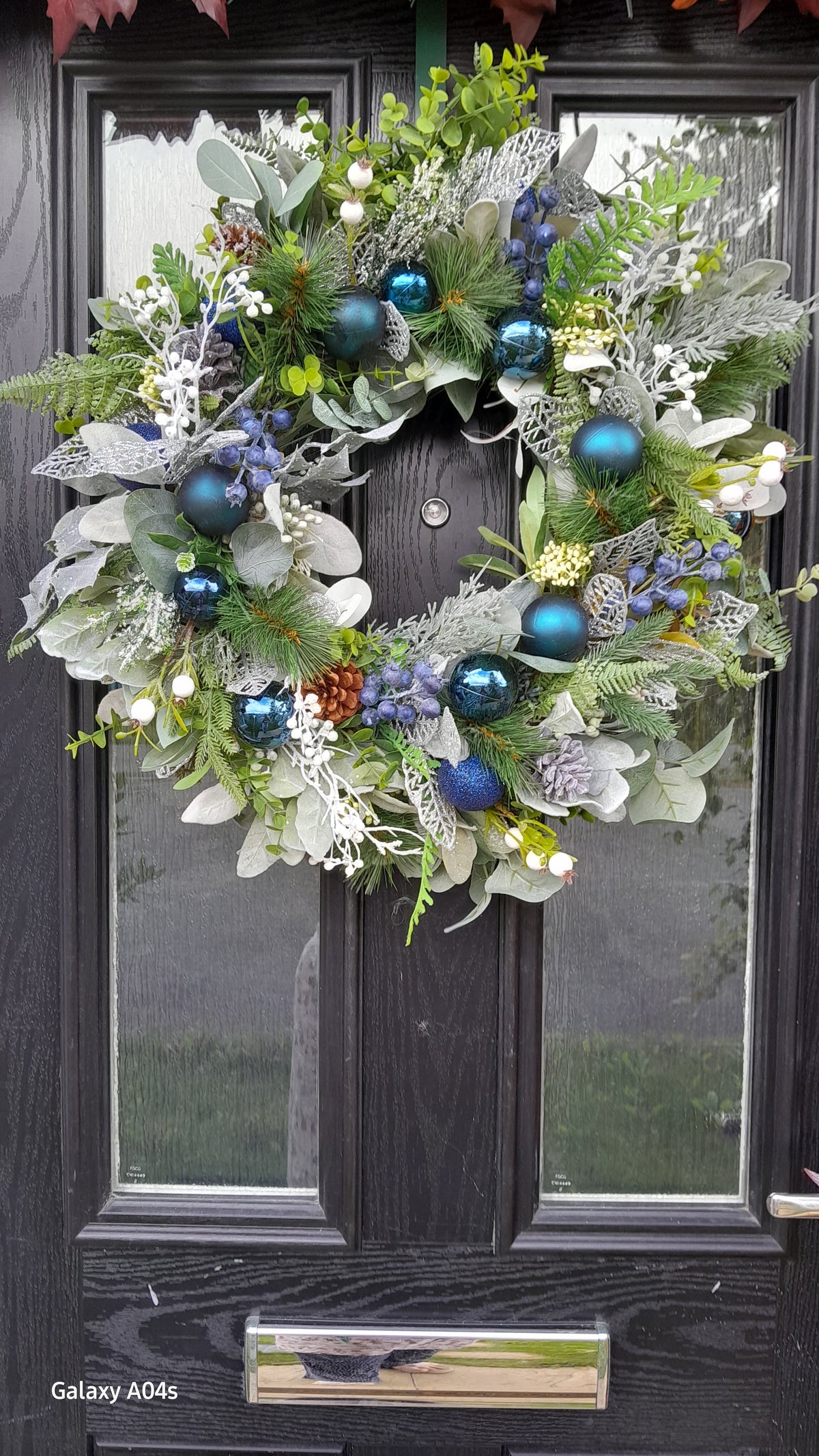 Blue and silver Christmas wreath hung on black door, slightly wider view