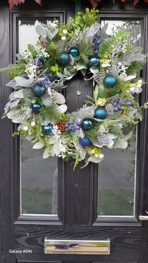 Blue and silver Christmas wreath hung on black door, slightly wider view