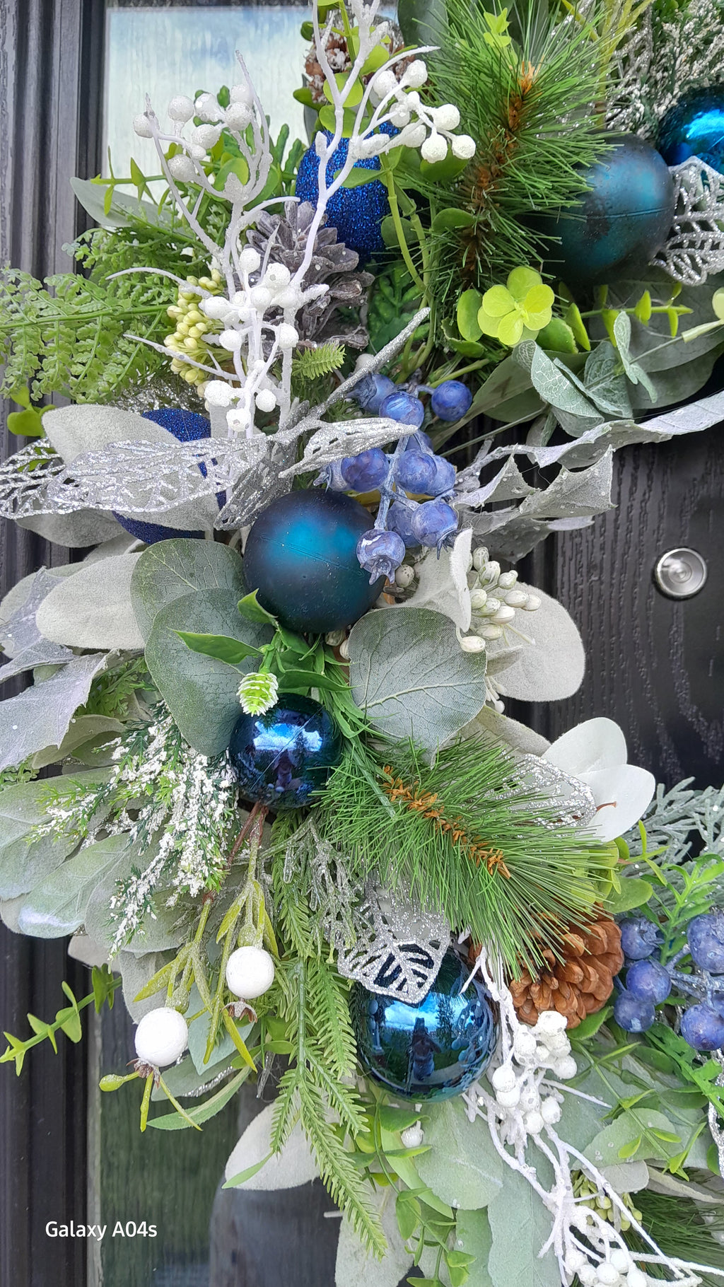 Close-up detail of blue Christmas wreath showing teal baubles, white berries and frosted foliage