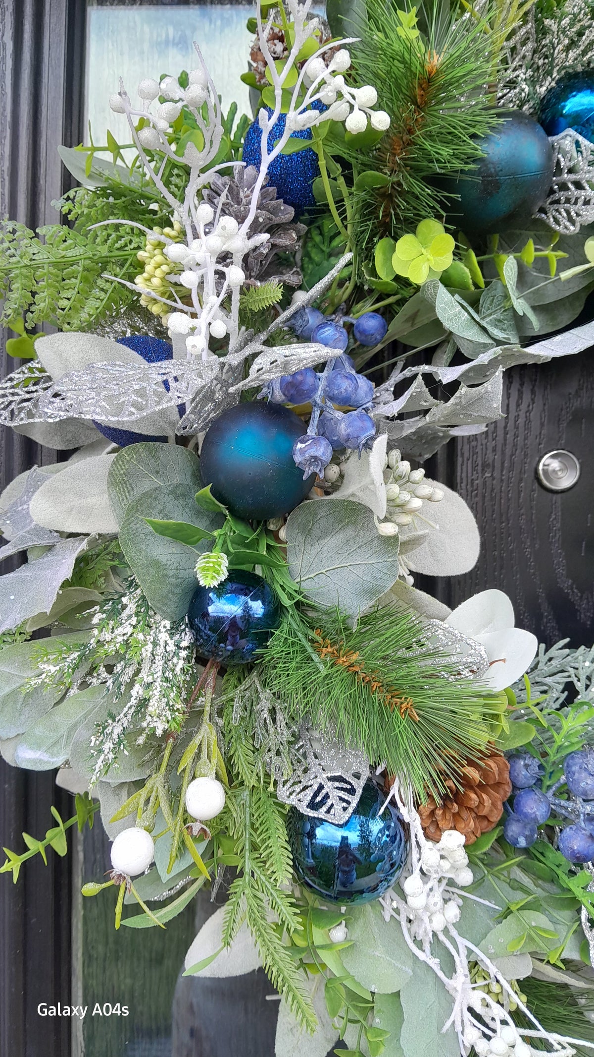 Close-up detail of blue Christmas wreath showing teal baubles, white berries and frosted foliage