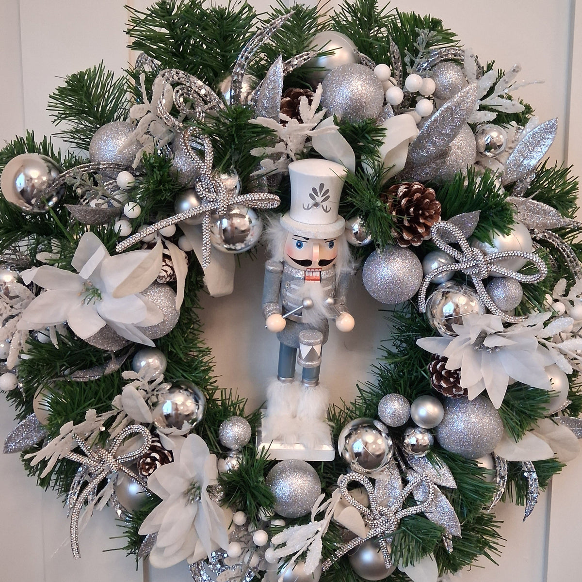 Lumi 22-inch Christmas wreath with silver nutcracker, silver baubles, sparkling bows and white flowers on green foliage