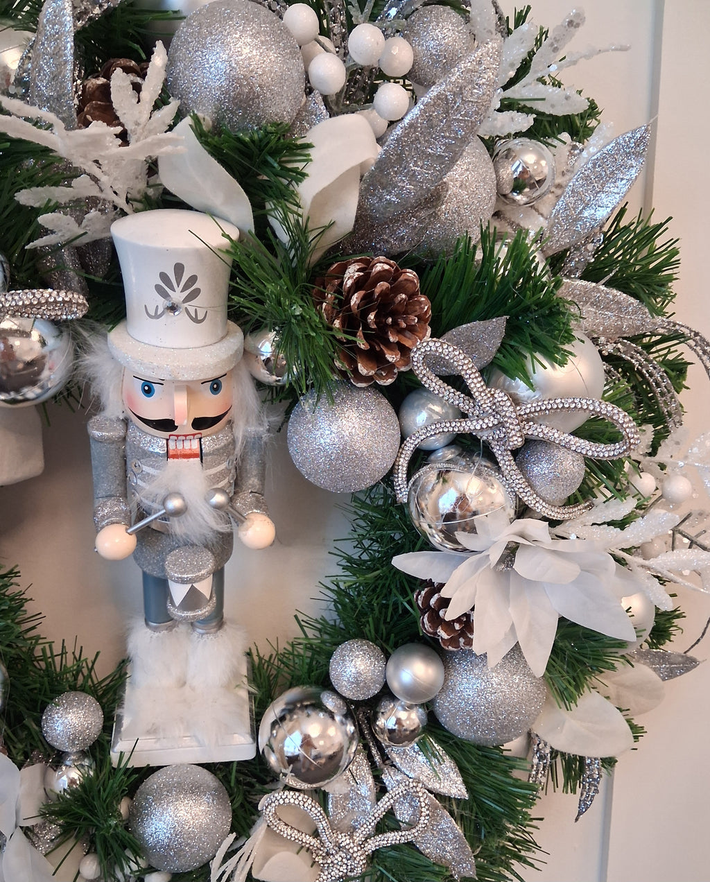 Close-up of silver nutcracker, glittered baubles, pine cones and sparkling bow on Lumi Christmas wreath