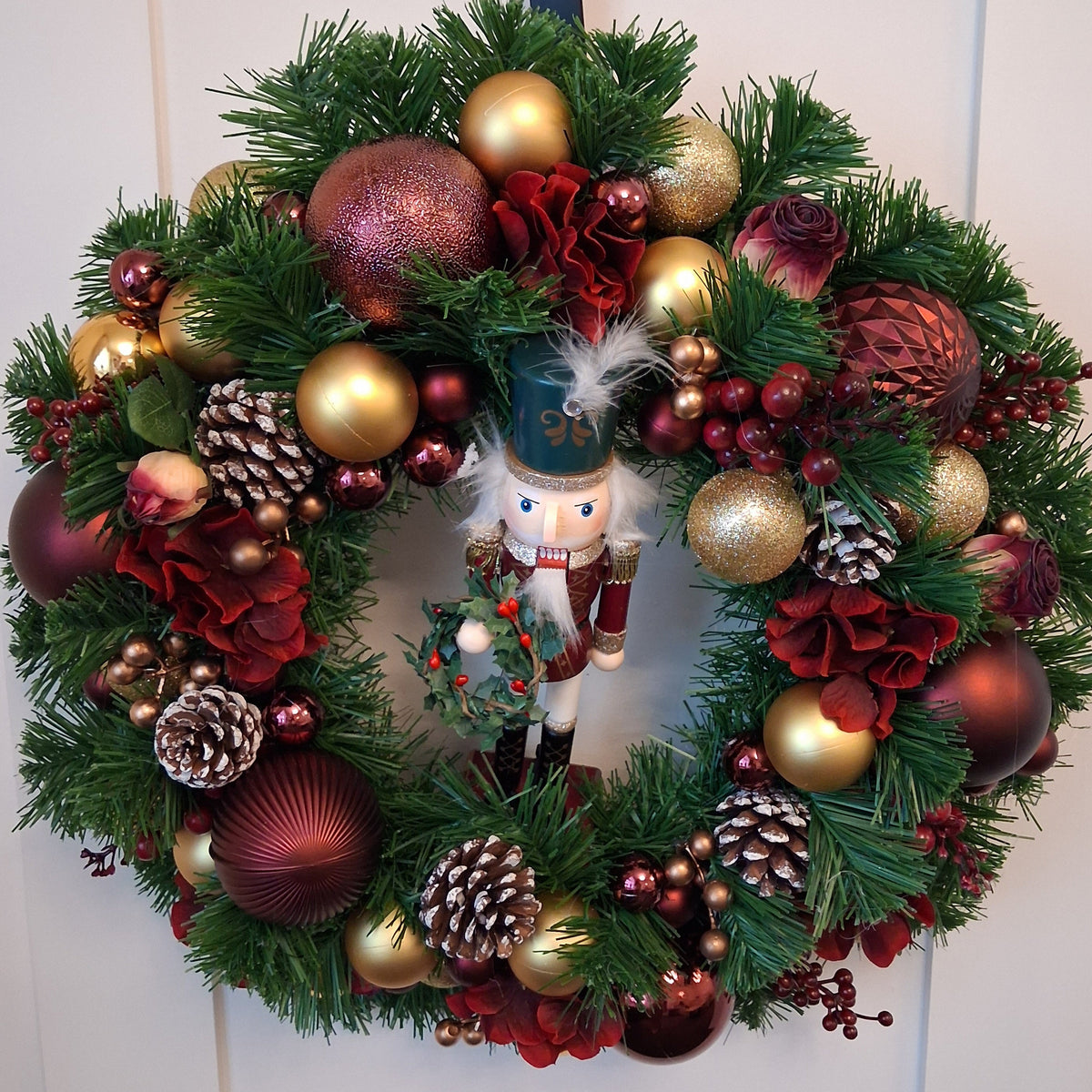 Vespera 20-inch burgundy and gold Christmas wreath with nutcracker, baubles, flowers and white-tipped pine cones