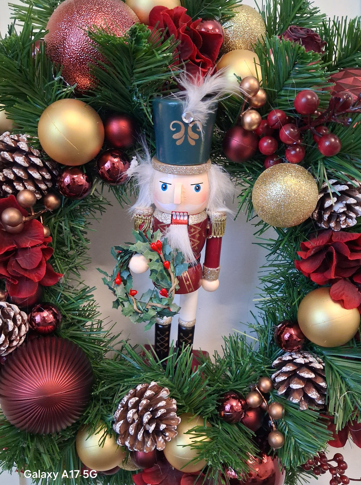 Close-up of Vespera nutcracker holding a miniature wreath among burgundy and gold baubles
