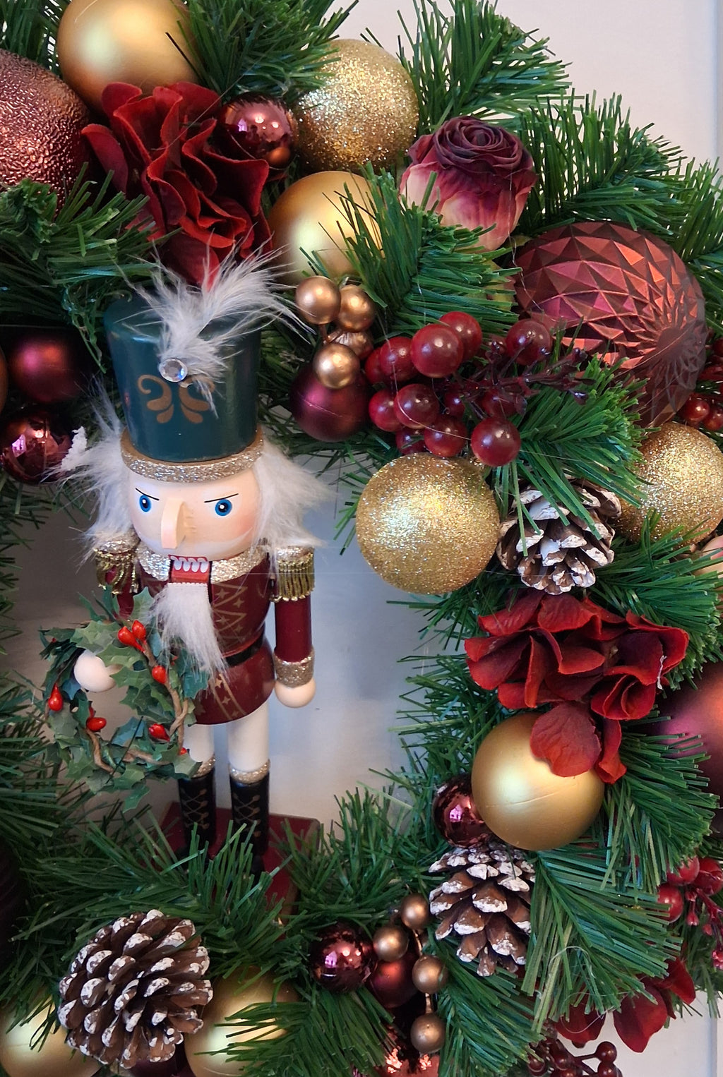 Detail of burgundy flowers, gold baubles, berries and pine cones on Vespera nutcracker Christmas wreath
