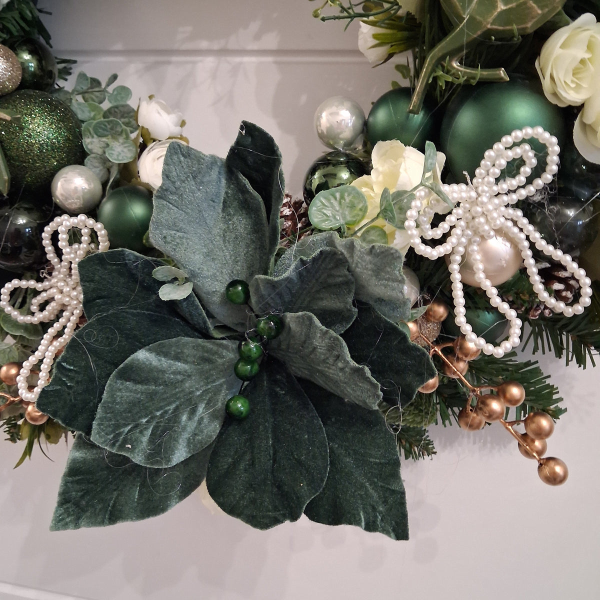 Deep green floral detail and pearl-style bows on emerald Christmas wreath