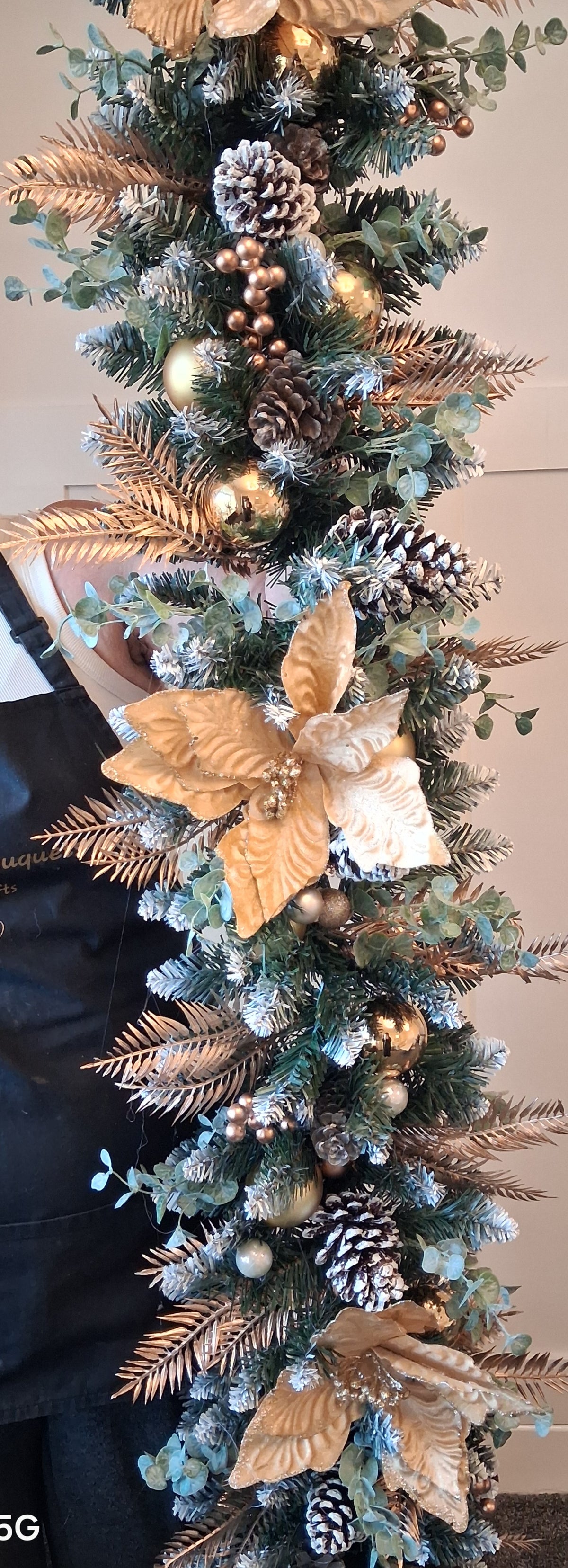 Gold and white Christmas garland detail with pine cones, baubles and green foliage