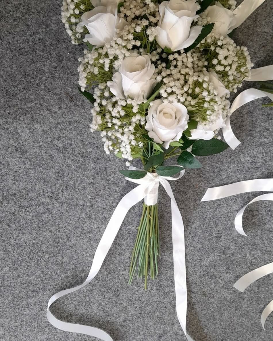 Ottilie bouquet laid flat - white roses and gypsophila with trailing white satin ribbon on hessian