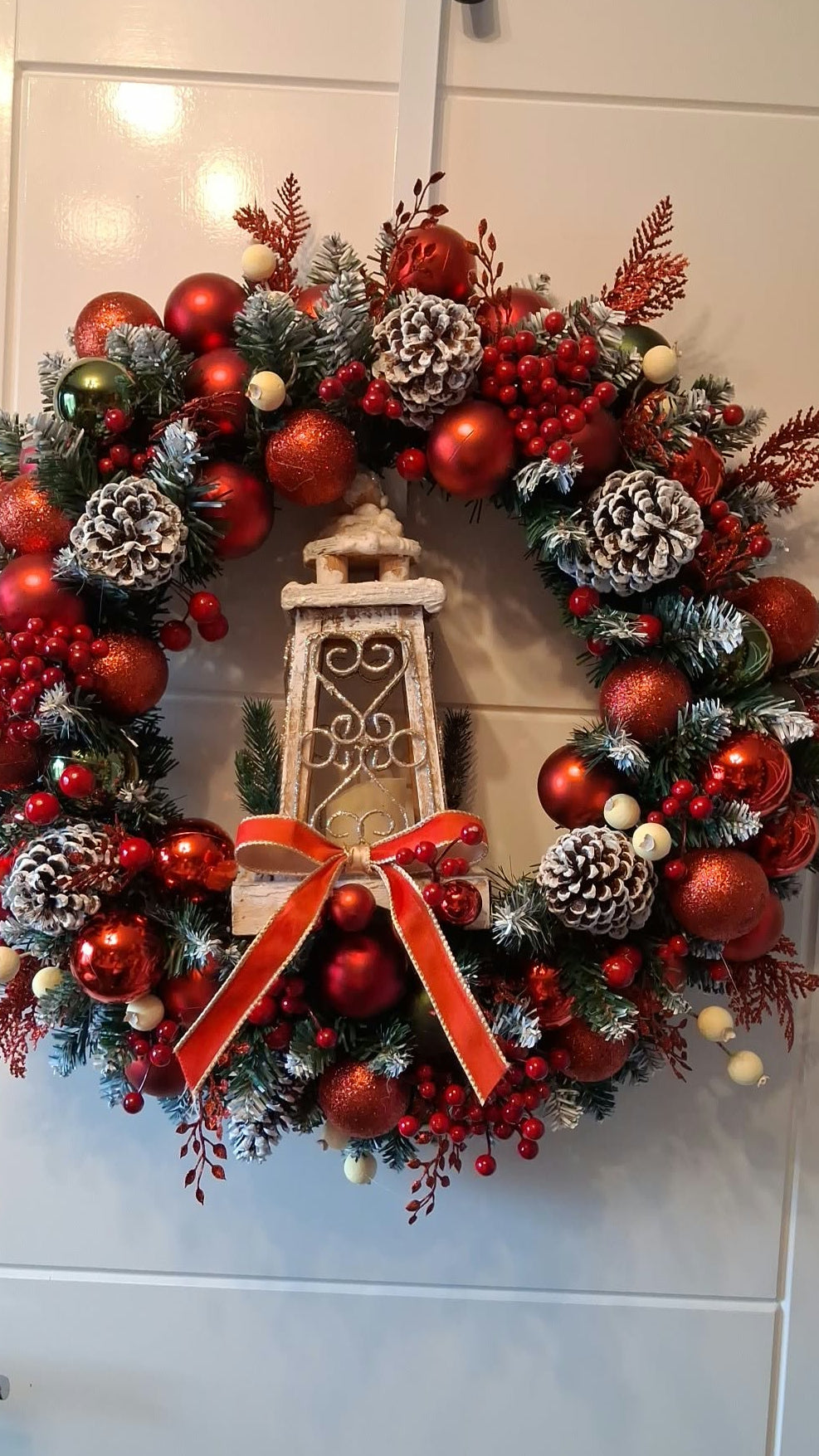 24-inch Christmas wreath with red and gold baubles, frosted pine cones, berries, a red bow and a central decorative lantern with a light-up faux candle