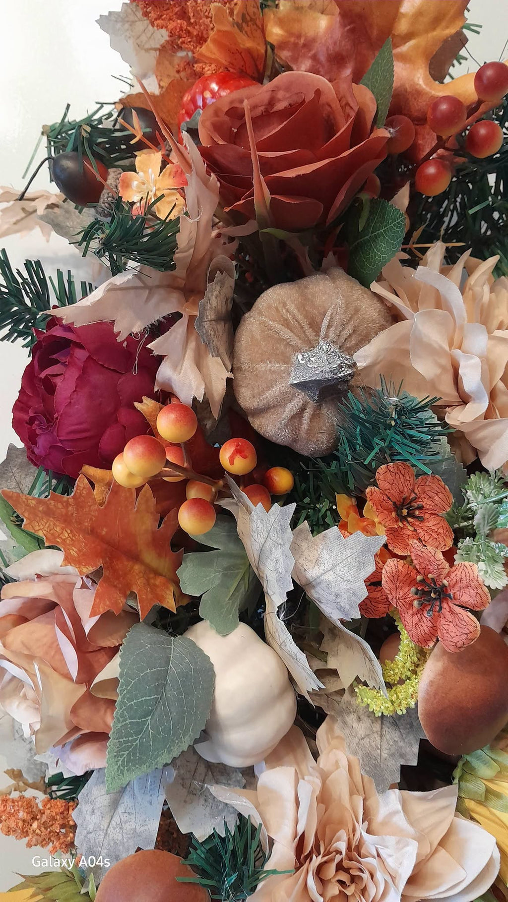 Close up detail of autumn garland featuring terracotta roses, burgundy peonies, glitter pumpkin and orange berries