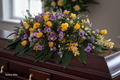 Double ended casket spray with yellow roses, purple lisianthus, gerberas and green foliage on a dark wooden casket