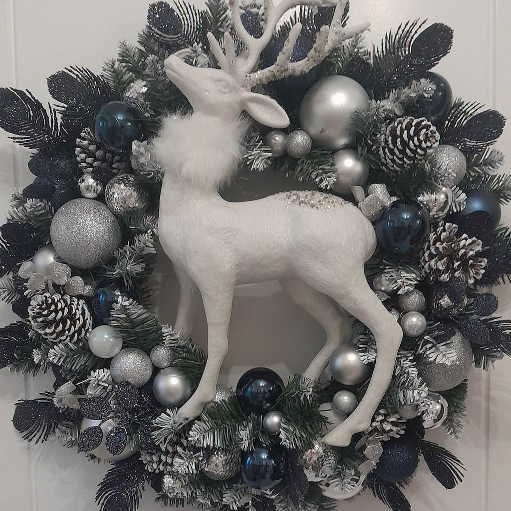 Midnight Stag Christmas wreath with white stag, navy and silver baubles and frosted pinecones on a pale door